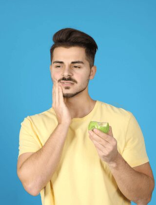 Man holding the side of his face after biting an apple