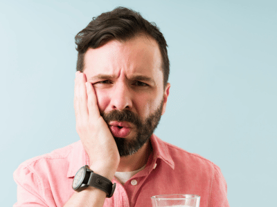 Man holding the side of his face from gum sensitivity between his teeth
