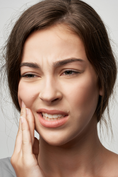 A woman with a toothache presses her fingers on the side of her face.