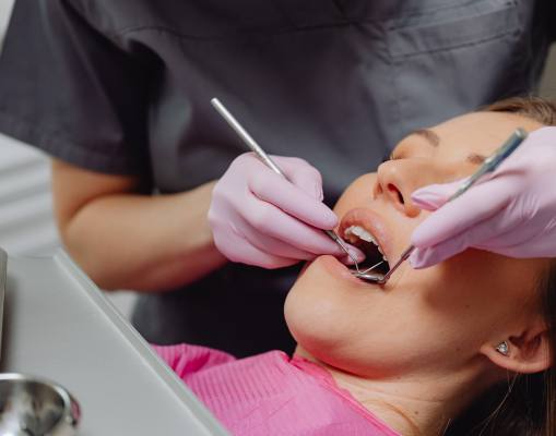 A dental hygienist's hands gently inserting tools in a patient's mouth